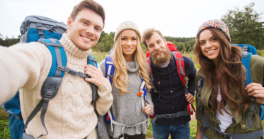 group of smiling friends with backpacks hiking