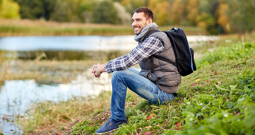 smiling man with backpack resting on river bank